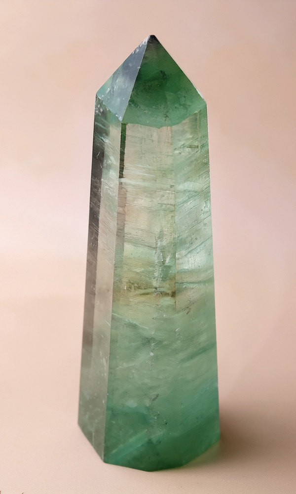 Ein Heilstein: grüner Fluorit in Form eines Obeliskes auf rosa Untergrund